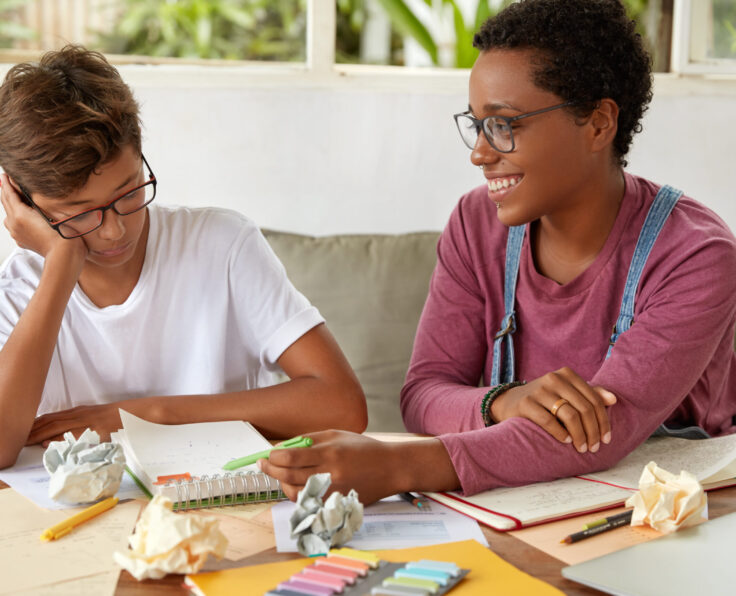 Image of mixed race boy and girl collaborate for preparing course paper, make records in notepad, sit at couch, work on presentation for class, being team. Learning and collaboration concept